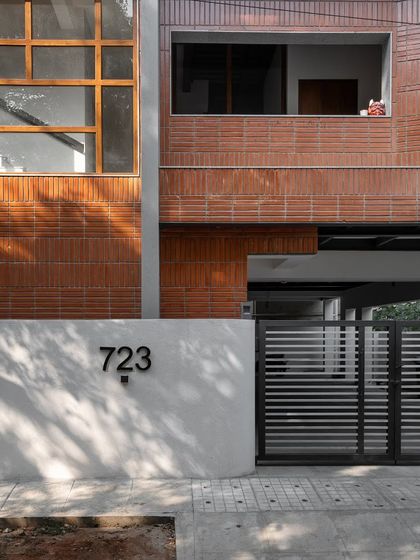 A closer look at the entrance of Project 723. The combination of the smooth white compound wall, the modern gate, and the textured brick facade creates a study in contrasts.