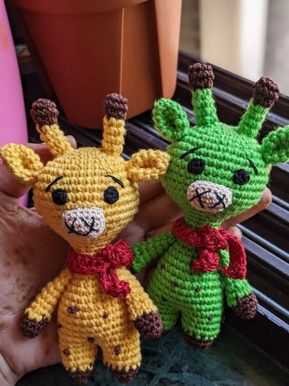 Two little giraffe friends, one yellow and one green, both with cozy red scarves.