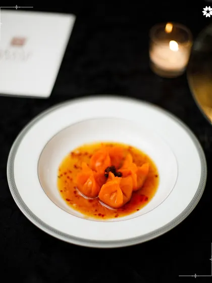 Vibrant orange dumplings served in a flavourful broth. The presentation is clean and modern, allowing the colours and textures of the dish to stand out.