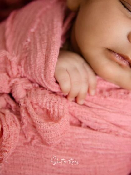 A macro shot focusing on the details of a pink wrap with a bow knot and the baby's tiny hand.