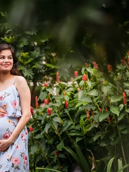 The maternal glow is real. This outdoor maternity portrait captures an expecting mother in a beautiful floral dress, surrounded by lush greenery and flowers. The natural setting complements the natural beauty of pregnancy.