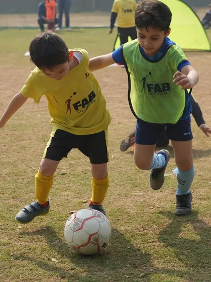 A young player shields the ball from a defender. This image shows the competitive but supportive environment we create, where players challenge each other to improve.