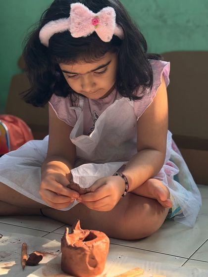 A young girl carefully works on her clay pot, demonstrating the development of fine motor skills and hand-eye coordination. Every pinch and roll is a step in her creative journey.