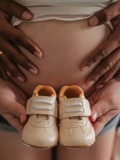 A close-up shot focusing on the baby bump, framed by the parents' hands holding a pair of tiny sneakers. This is a beautiful and symbolic way to celebrate your growing family.