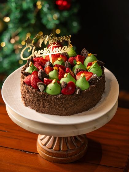 The Rich Chocolate Strawberry cake decorated for Christmas. It's topped with fresh strawberries, mini Oreos, and festive green cream, making it a delightful holiday treat.