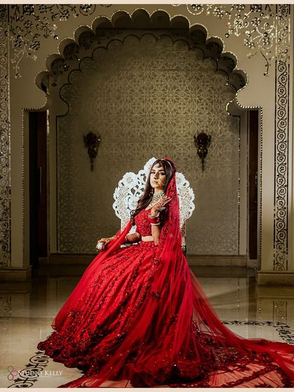 A regal bridal portrait of the bride seated on an ornate silver throne, looking every bit like a queen in her stunning red lehenga.
