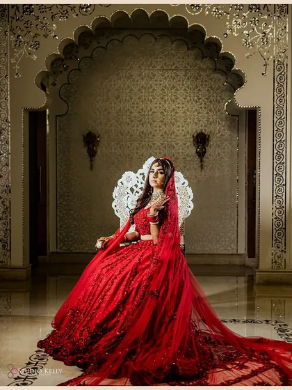 A regal bridal portrait of the bride seated on an ornate silver throne, looking every bit like a queen in her stunning red lehenga.