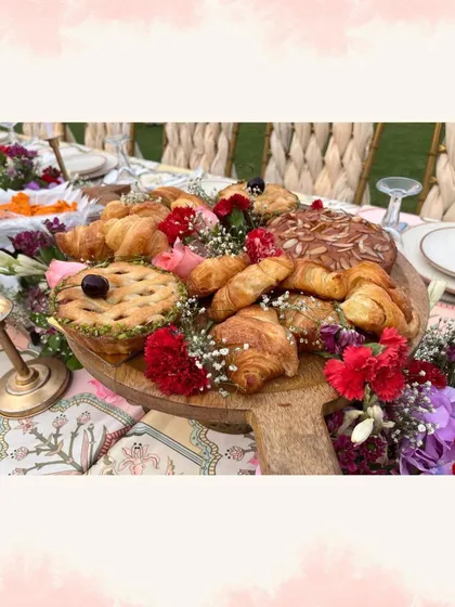 A beautiful grazing platter of fresh croissants, pies, and pastries, decorated with flowers, for a brunch event.