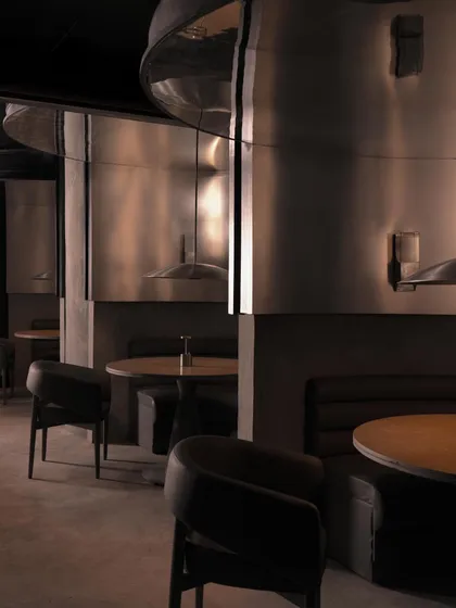 Intimate seating pods are defined by curved stainless steel backrests. The reflective surfaces create a dialogue with the surrounding darkness, offering glimpses of movement and light.