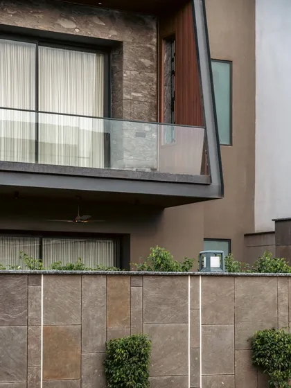 A detail of the Club Drive House facade, where a cantilevered balcony with a glass railing adds a sense of lightness to the solid stone and wood structure.
