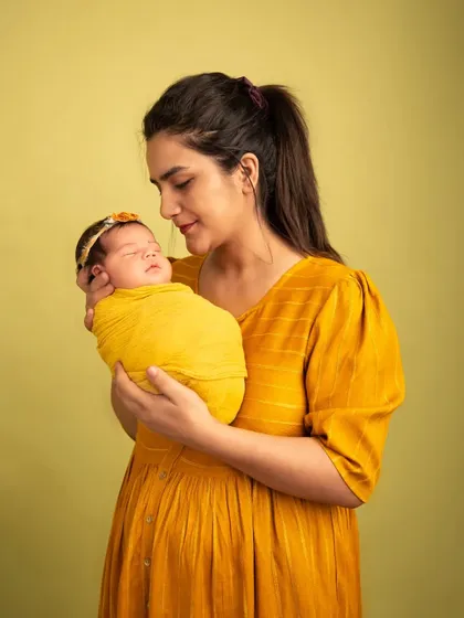 A mother's gentle gaze. The coordinated colors of the mother's dress and the baby's wrap create a visually harmonious portrait that emphasizes their connection.