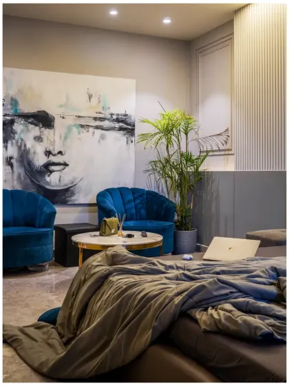 A cozy reading corner within a bedroom. The plush blue chairs provide a pop of color against the neutral grey walls, while the large abstract painting adds a layer of artistic sophistication.