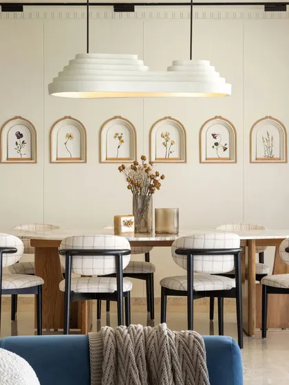 The dining space is all about harmony. An organic-shaped marble table is illuminated by a custom-made layered light installation, surrounded by comfortable black-stained dining chairs. The accent wall features niches with delicate, hand-painted floral artwork, adding a personal and artistic touch.