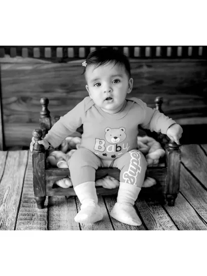 A black and white portrait of baby Navya, one of the six-month-old twins. The wooden backdrop and floor add rustic texture to this sweet and simple baby photo.
