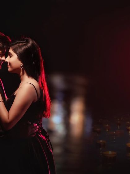 A close, intimate portrait of a couple at night, with diyas floating on the water in the background. The warm, soft lighting creates a deeply romantic and slightly spiritual mood.