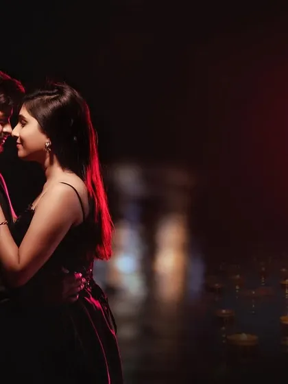 A close, intimate portrait of a couple at night, with diyas floating on the water in the background. The warm, soft lighting creates a deeply romantic and slightly spiritual mood.
