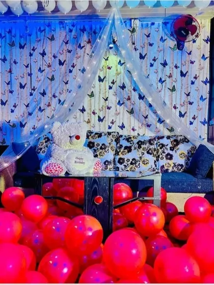 A whimsical room decoration with a butterfly theme. A canopy over the sofa is surrounded by red balloons and a teddy bear, creating a playful and romantic vibe.