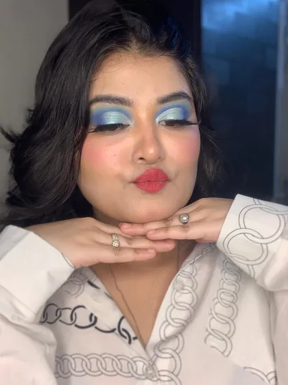 A playful pose showing off the full effect of the vibrant blue eyeshadow and red lip.