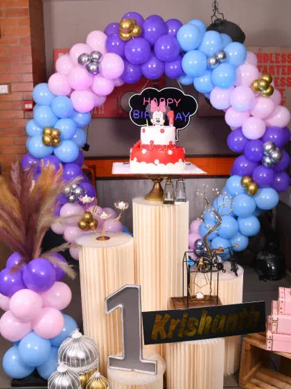 A classic Minnie Mouse theme for a first birthday. The balloon arch in shades of purple, blue, and pink frames the cake stand, creating a beautiful focal point for the celebration.