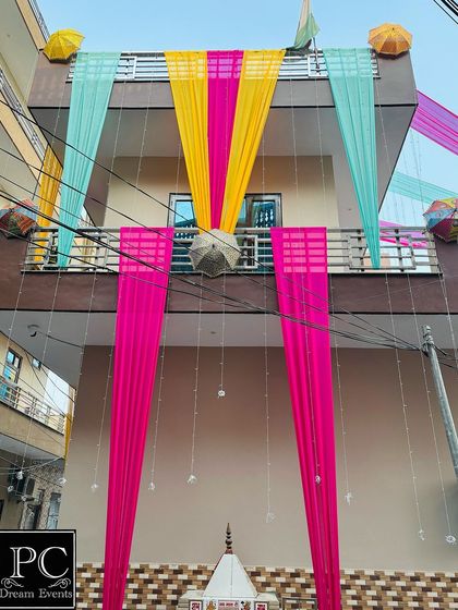 Another angle of the colorful home exterior decoration. The combination of pink, yellow, and turquoise drapes creates a joyful and unmissable announcement of the wedding festivities.