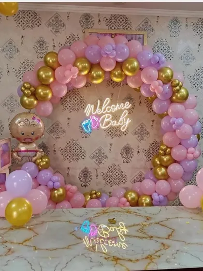 A beautiful "Welcome Baby" arch in shades of pink, purple, and gold. This setup includes a neon sign, 'BABY' blocks, and a baby girl foil balloon, perfect for a tabletop display.