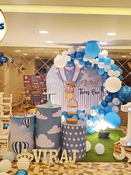 A charming hot air balloon-themed first birthday. The setup includes hot air balloon cutouts, a 'VIRAJ' marquee, and a large light-up number '1'.