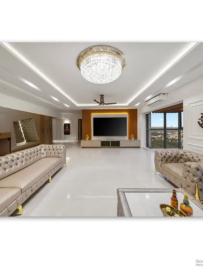 A wide view of a luxurious living room in Tata Aquelia Heights, featuring plush tufted sofas and a grand crystal chandelier. The expansive layout and pristine white marble floors reflect a sense of opulence and modern grandeur.