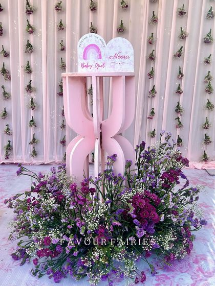 A sweet and simple detail from a baby girl's welcoming ceremony. A personalized sign for baby Noora sits on a modern pink pedestal, surrounded by fresh flowers.