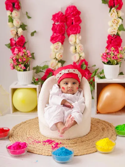 Another shot from the Holi festival setup, capturing the baby looking curiously at the camera, with a small dot of color on his cheek.