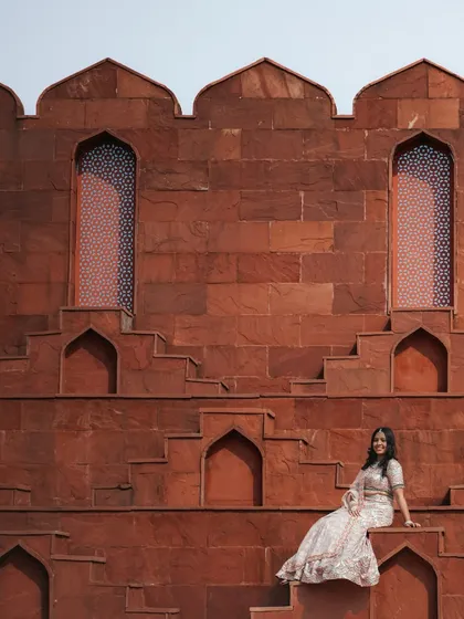 A stunning solo portrait of the bride seated against the unique geometric patterns of a red sandstone step-well wall, highlighting her elegant lehenga.
