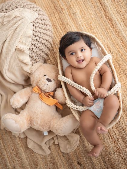 A baby girl playing with a teddy bear in a basket.