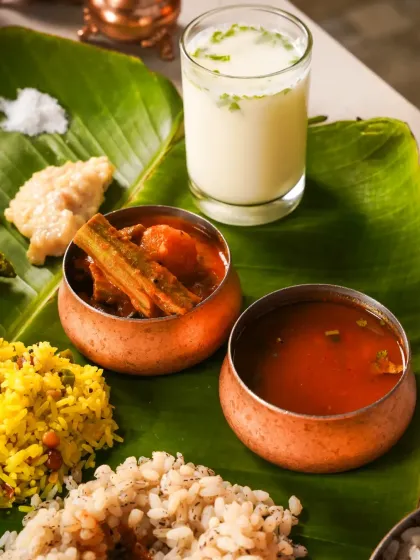 A close-up of a traditional Onam Sadhya meal, focusing on the sambar, rasam, and buttermilk served in copper bowls on a banana leaf. This shot highlights the authentic serving style.