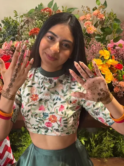 A happy bride showing off her minimal mehendi. The design features delicate floral vines and dotted patterns on the palms, creating a fresh and classy look that matches her vibrant personality.