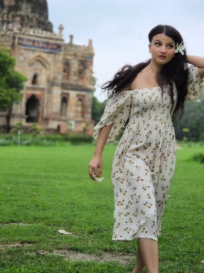 A candid walking shot that captures movement and personality. The composition uses the tree to frame her, with the Lodi Garden tomb creating a classic backdrop.
