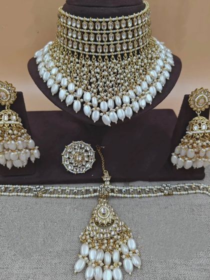 A stunning gold and pearl Kundan set with a wide choker, heavy jhumkas, and a matching maang tikka and ring.
