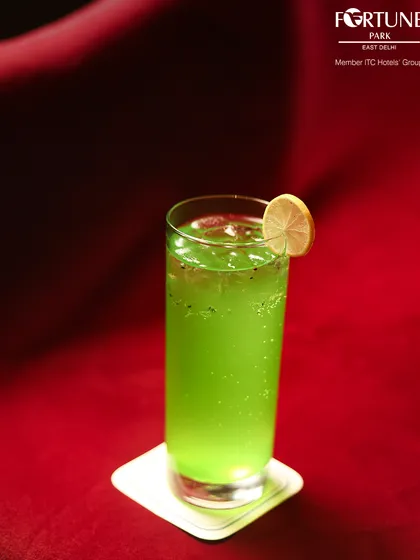 A vibrant green mocktail, served against a rich red backdrop, showcasing the bold colors and refreshing flavors of our non-alcoholic beverage selection.