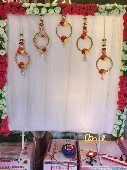 A simple and elegant rectangular backdrop frame decorated with white cloth, floral borders, and hanging ornaments. This versatile frame can be customized for any festival.