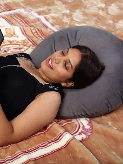 A model relaxing in bed while using her phone, with her head resting on a grey neck pillow. This shows the product's utility for everyday relaxation.