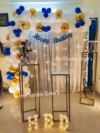 A simple balloon arch in blue, white, and gold against a curtain with fairy lights. This is a classic and elegant choice for a home birthday party.