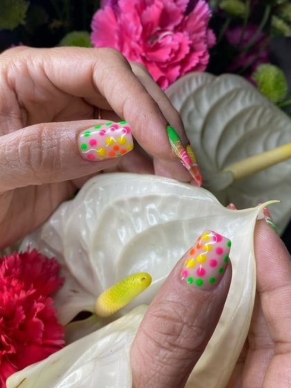 A close-up of the vibrant neon polka dot nails, held against beautiful flowers that complement the colors.