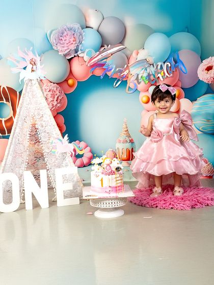 Standing tall and proud at one year old! This little girl's joyful expression and beautiful pink dress light up the entire studio during her first birthday photoshoot.