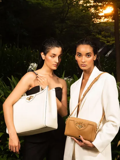 A fashion-forward portrait of two models for Koxoxo. The dramatic lighting and lush green background create a high-end, luxurious feel for this handbag campaign.