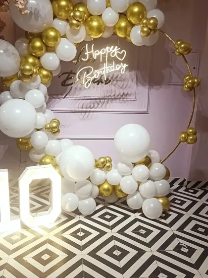 Here is a simple yet very classy ring decoration for a 10th birthday party at home. The white and gold chrome balloons, paired with a neon sign and light-up numbers, create a sophisticated look for a milestone celebration.