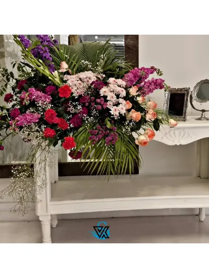 A large, dramatic floral arrangement on a white console table creates a beautiful welcome point for guests, combining various shades of pink, purple, and peach.