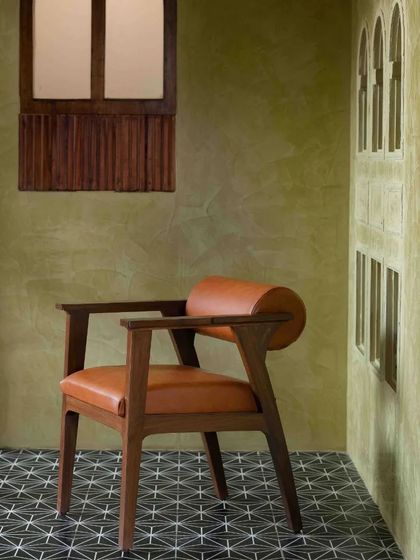 A custom-designed armchair in teak and tan leather. The cylindrical backrest adds a modern touch to the classic form, reflecting the restaurant's design philosophy.