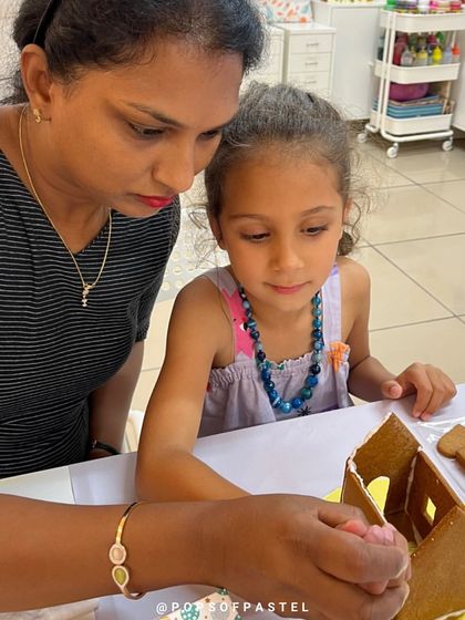 An instructor helps a young girl get started on her gingerbread house, showing her how to apply the icing.