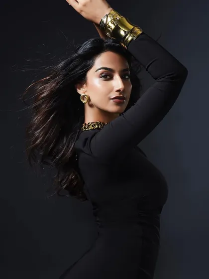 A powerful and dynamic pose in a sleek black dress. The styling is elevated with bold gold accessories, creating a look that is both strong and sophisticated.