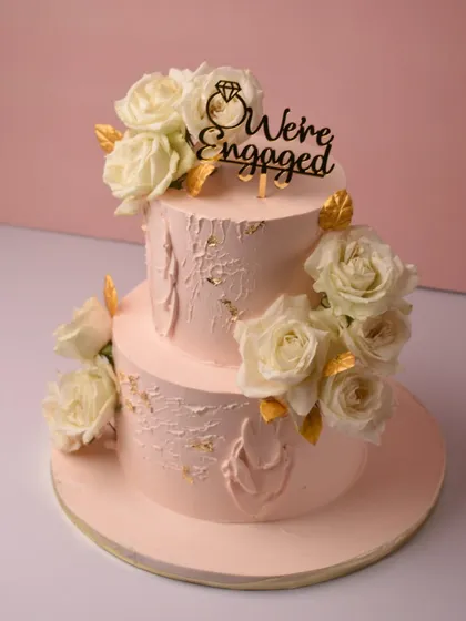 We created this beautiful two-tier engagement cake in just two hours, baking everything from scratch. It features a soft pink textured frosting, fresh white roses, and a "We're Engaged" topper to celebrate the happy couple.