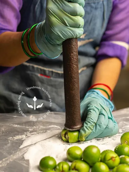 The traditional method of de-seeding gunda berries using a stone pestle. This careful process is essential to prepare them for stuffing.