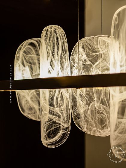 This linear pendant features organic, rounded glass elements with a beautiful white smoke effect inside. Suspended from a simple gold bar, it provides a soft, ethereal glow, ideal for creating a serene atmosphere over a dining table.